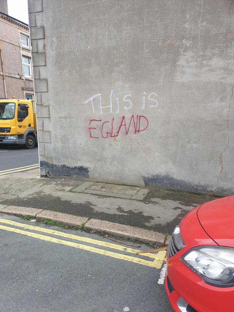 White and red graffiti on a wall, it says "THIS IS EGLAND", yes it is spelt Egland. 