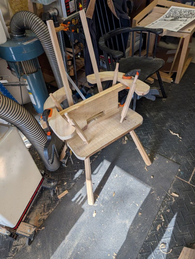 a partially assembled unfinished wooden chair with parts held together by clamps