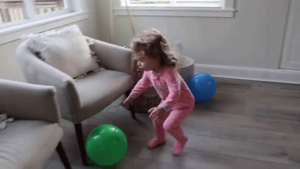 a little girl is playing with balloons in a living room next to a couch .