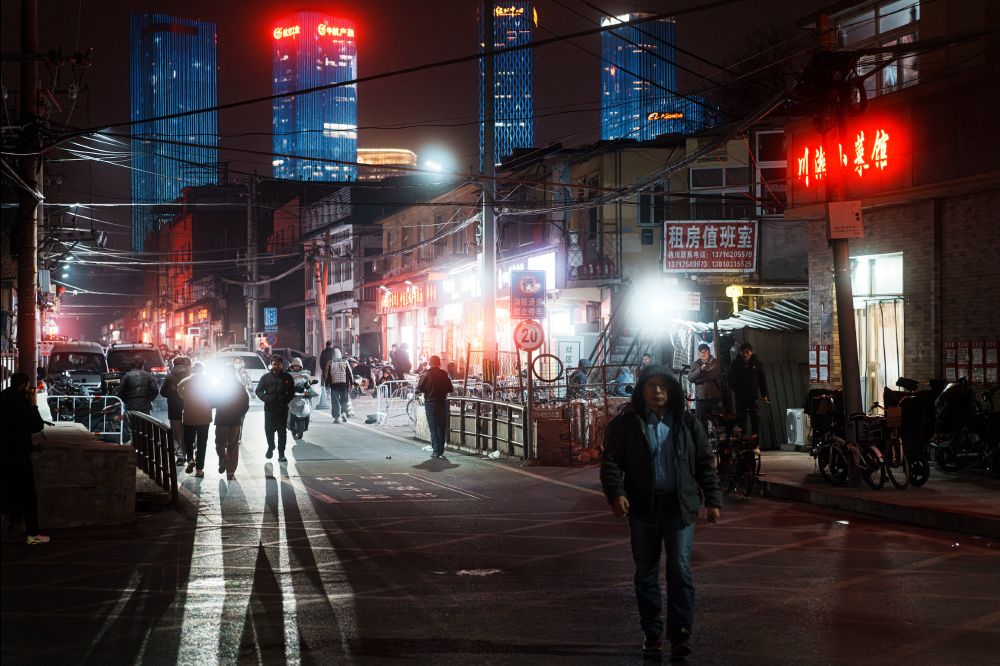 Beijing street photography in color, night scene of backlit men walking and big towers in the background