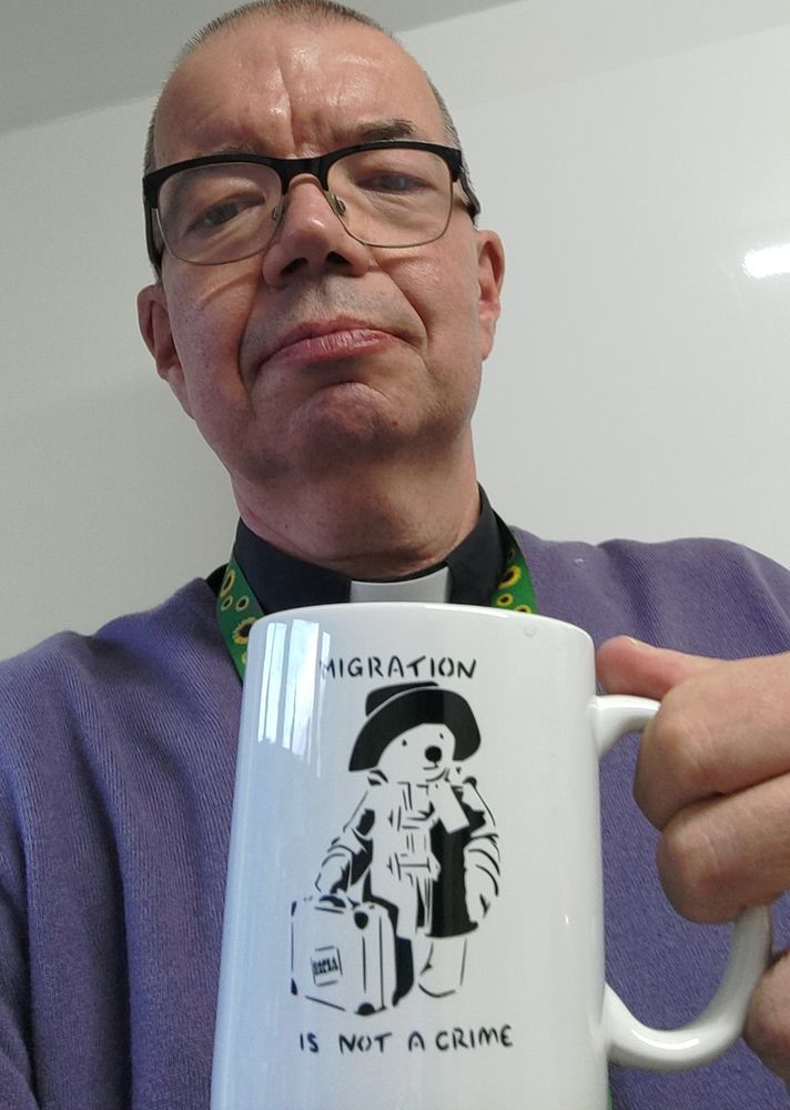 A Vicar with a mug saying Immigration is not a crime and the image of Paddington 