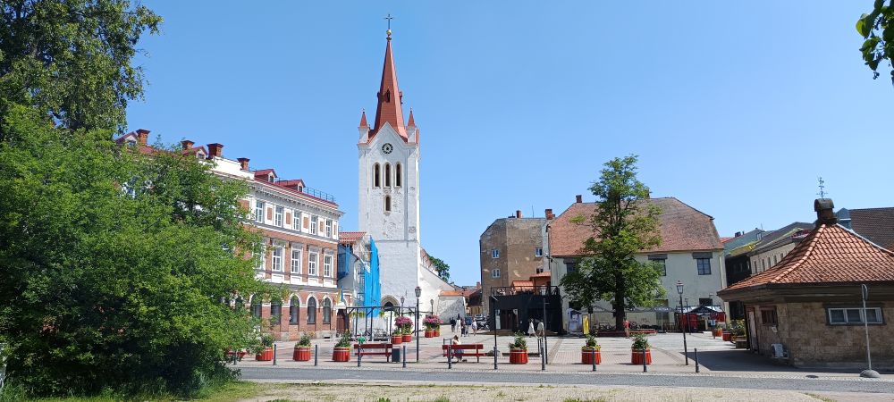 Rose square is pictured on a sunny day, in the centre of the old castle town Cēsis, Latvia. The Lutheran church has an open day, today. In the front is a water fountain.