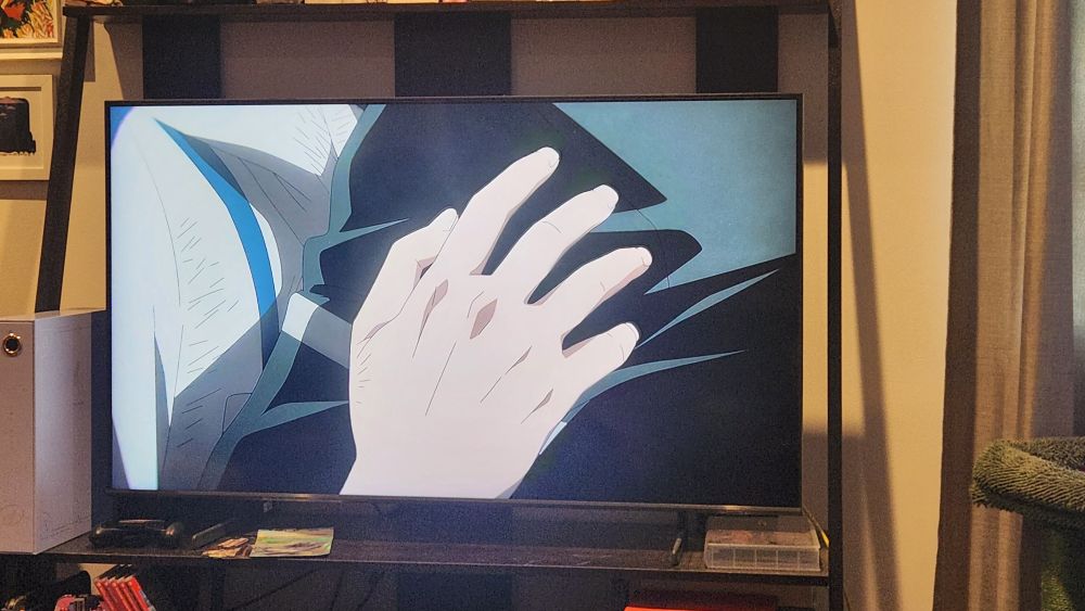 A TV paused on season 2, episode 16 of Wind Breaker anime where two young men are hugging post high school delinquent brawl battle. There is a close up of a hand holding an arm tightly.