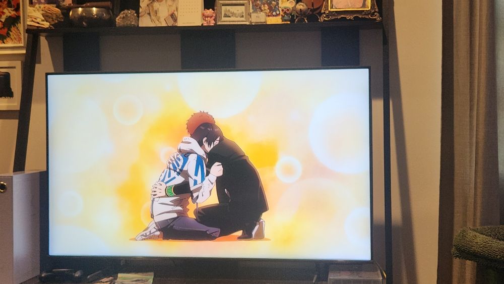 A TV paused on season 2, episode 16 of Wind Breaker anime where two young men are hugging post high school delinquent brawl battle. 
