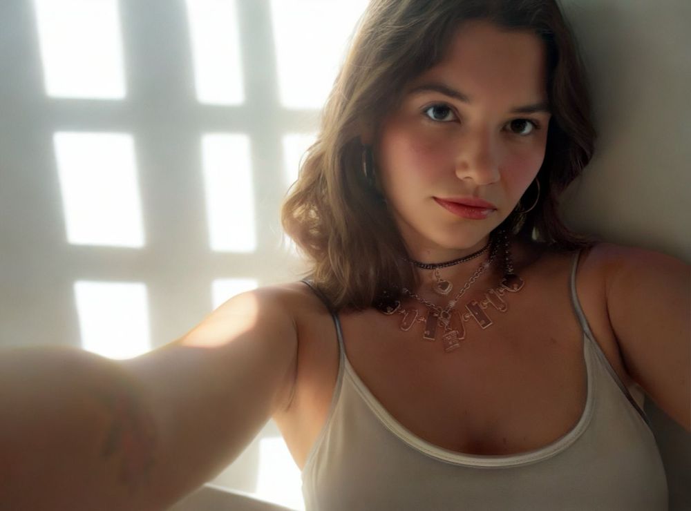 Selfie in a grey tank top and layered vintage necklaces.