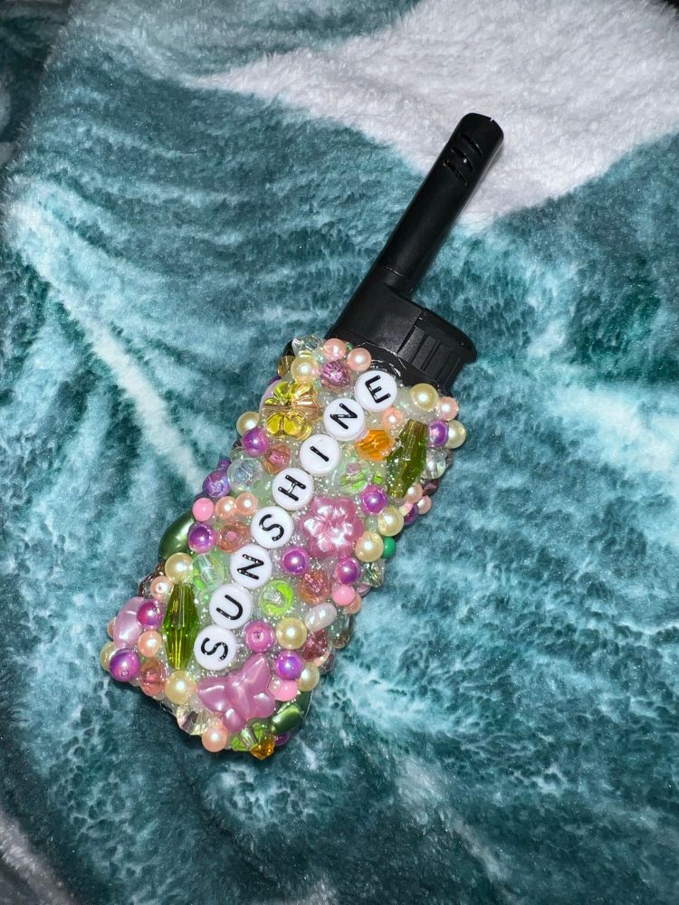 A BIC lighter covered in sparkly and pearly beads with the word “sunshine” on it.