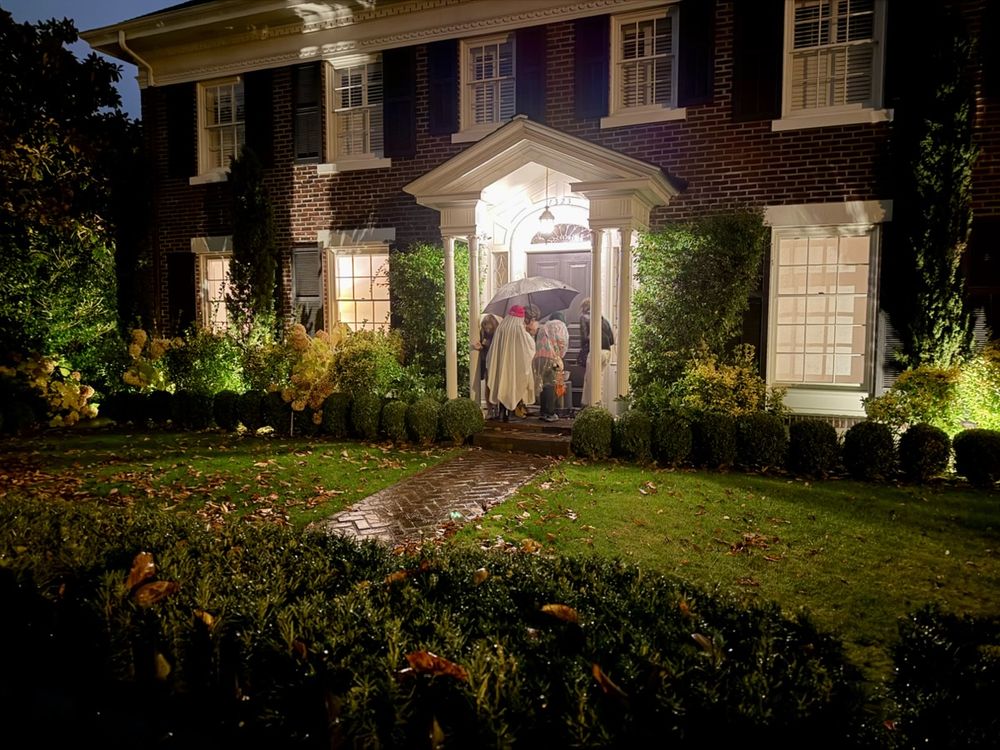 A group of kids trick or treating on the porch of a classic colonial style mansion.
