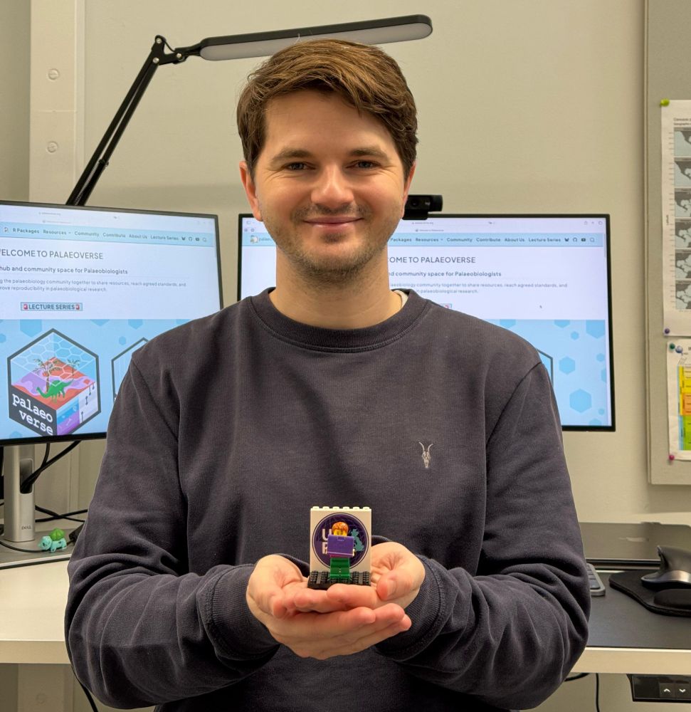 Lewis Jones, a smiling brown haired man, holding the lego minifigure of Dorothy Bishop (the 'Doscar' award for UKRN Dorothy Bishop Prize) out in front of him.
