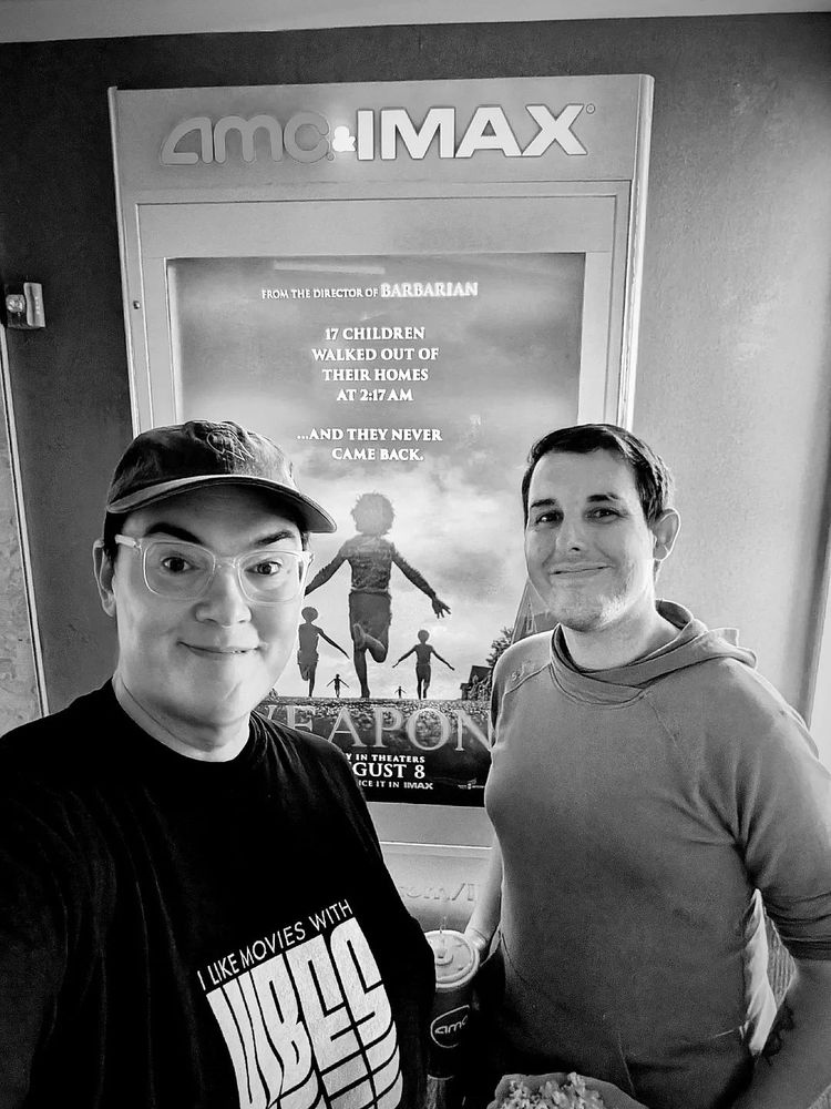 Mona and Val take a selfie in front of the IMAX poster for Weapons.