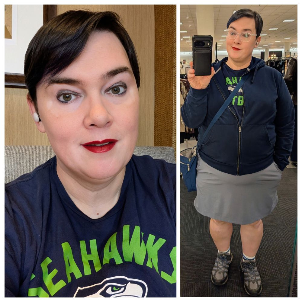 Mona has short dark hair with blue highlights. She is wearing glasses with transparent frames. She has on grey eyeshadow, navy eyeliner, Russian Red lipstick. She is wearing a navy hoodie over a navy Seattle Seahawks shirt. She is wearing a grey skirt, white socks with blue stripes, and grey & blue Eddie Bauer hiking shoes.