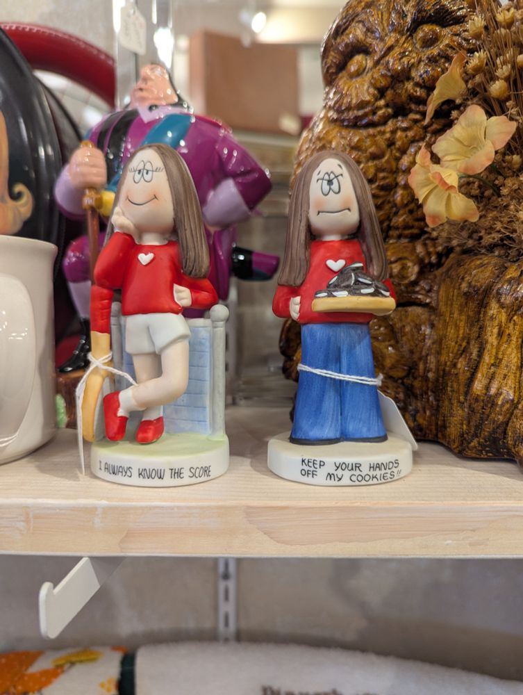 two Cathy comic strip figurines at an antique mall. One says "I always know the score" and the other says "Keep your hands off my cookies!" Also, this is irrelevant, but there's a statuette of Governor Radcliffe from Pocahontas standing behind them both on the shelf, looking like an absolute unit
