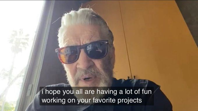 David Lynch wearing sunglasses looking down sat in front of Orange/Yellow cabinets captioned “I hope you all are having a lot of fun working on your favorite projects”