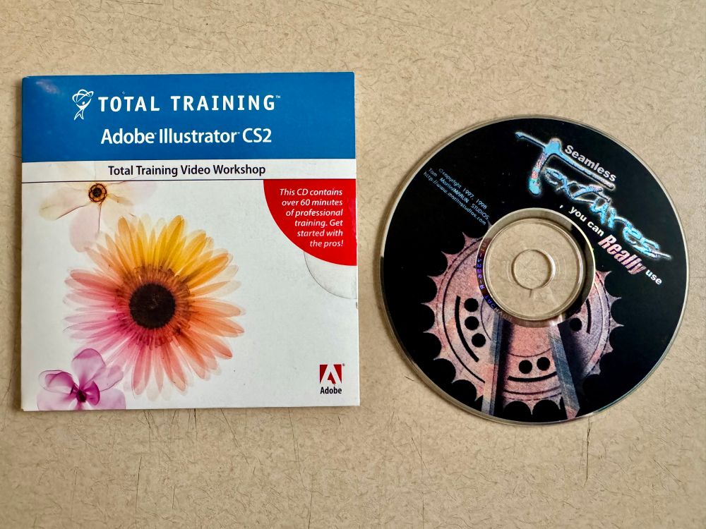 Two compact disc on a beige table. Left disc reads Total Training Adobe Illustrator CS2 and the right one says Seamless Textures you can really use