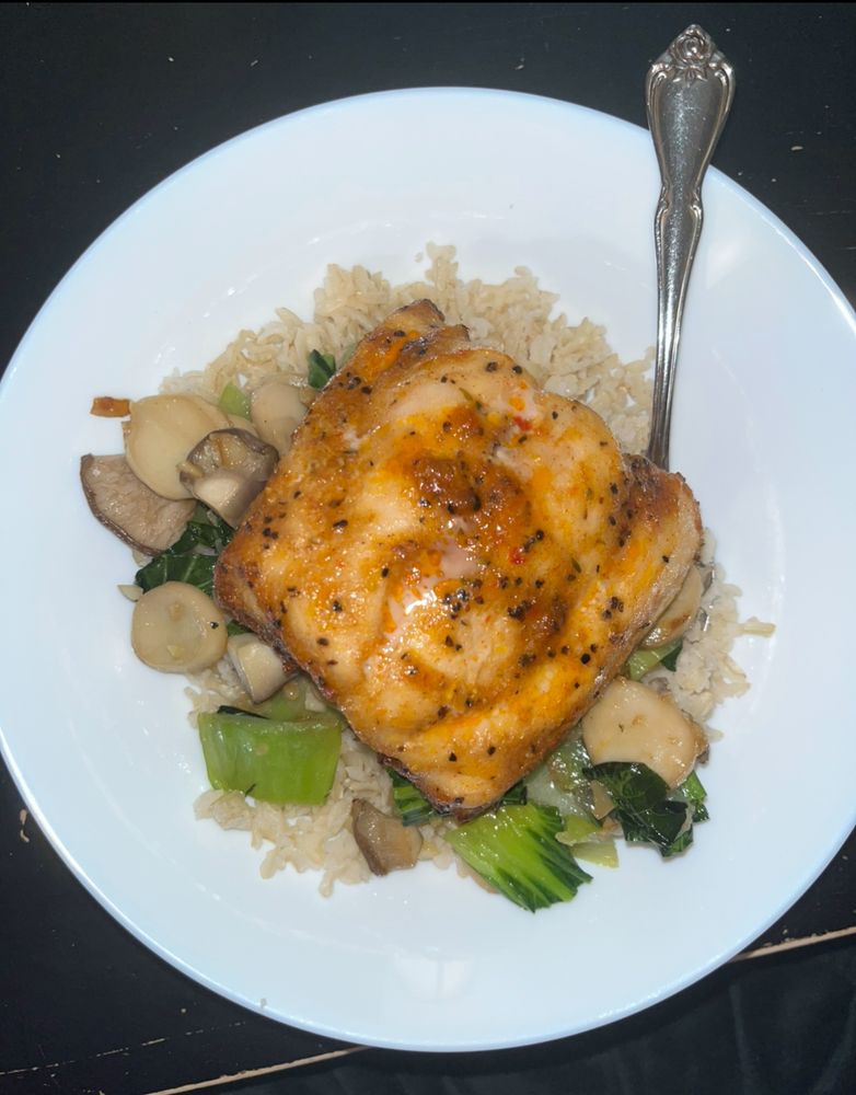 A photo of plated, seasoned salmon, on a bed of sautéd bok choy & mushrooms, all on brown rice.
