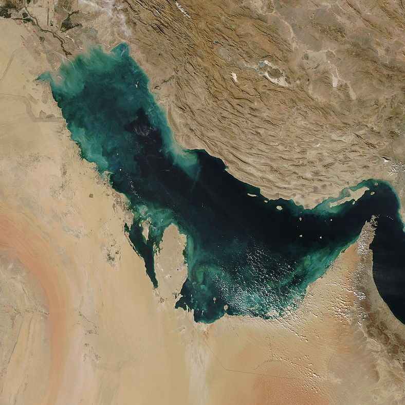 A satellite imagery of the Persian Gulf almost entirely sheltered by the surrounding Arabian Peninsula and Iran, with a small outlet at the Strait of Hormuz to the southeast