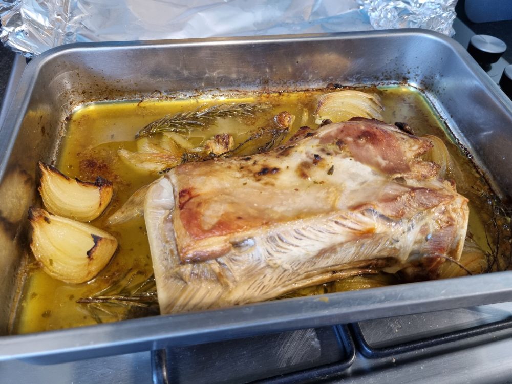 roasting tin with cooking stock (with onion, garlic, rosemary and thyme) and a shoulder of lamb joint fresh from the oven 