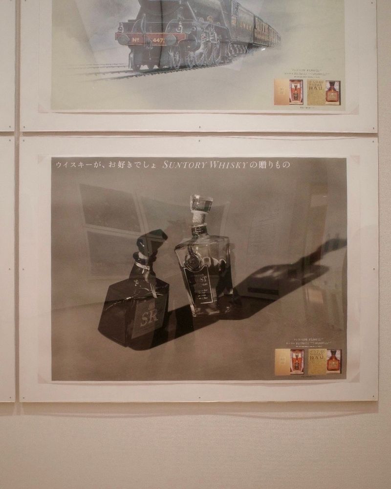 滋賀県立美《BUTSUDORI ブツドリ:モノをめぐる写真表現》展示風景。
サイズの異なるウイスキー瓶が二本寄り添うように並んだポスター。
ウイスキーが、お好きでしょ　SUNTORY WHISKYの贈りもの、のコピー。