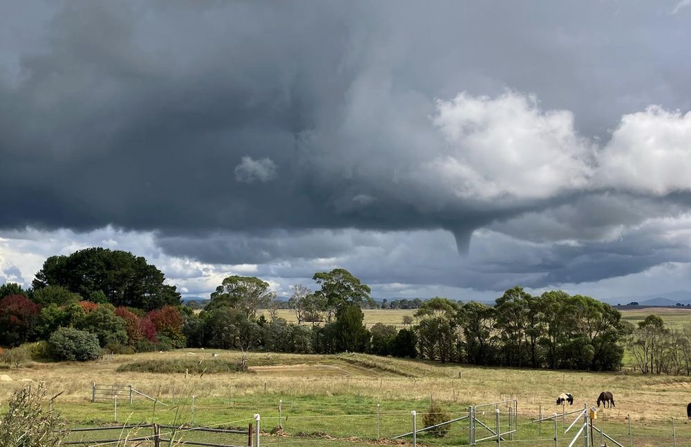 Stormy sky with tornado spout and green fields in foreground