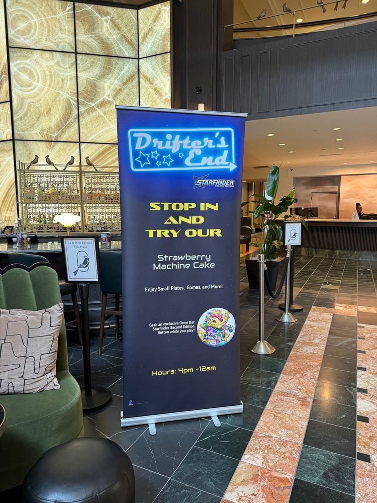 A sign at GenCon, which I am NOT ATTENDING, that says "Stop In And Try Our Strawberry Machine Cake"