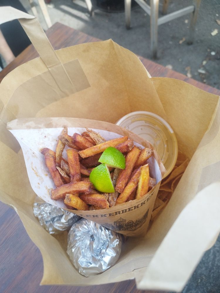 Blick in eine Papiertüte. Einige Sachen eingepackt. Sichtbar ist eine Tüte Pommes mit Limettenschnitzen drauf.