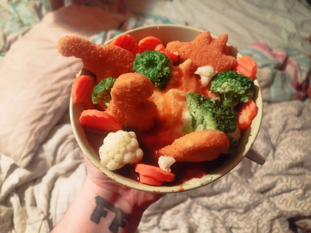 Eine Schüssel, im der ein Kartoffelpüreeberg, Dinonuggets, Brokkoli- und Blumenkohlbäume und Möhrenschollen sind. Alles ertränkt in einem Saucen-See