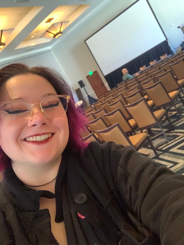 Woman with pink hair standing in front of an empty conference room