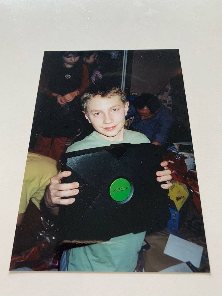 Moi enfant grand sourire tenant dans mes mains la première Xbox qui est plus large que mon torse.