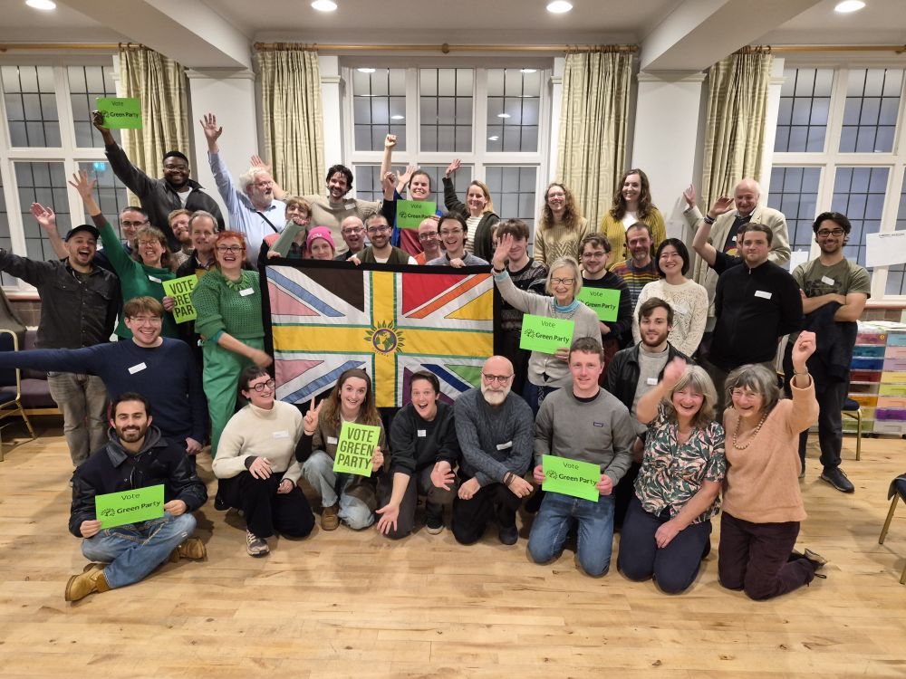 Huge group of 30+ green party members holding Vote Green signs and a unity union jack flag.