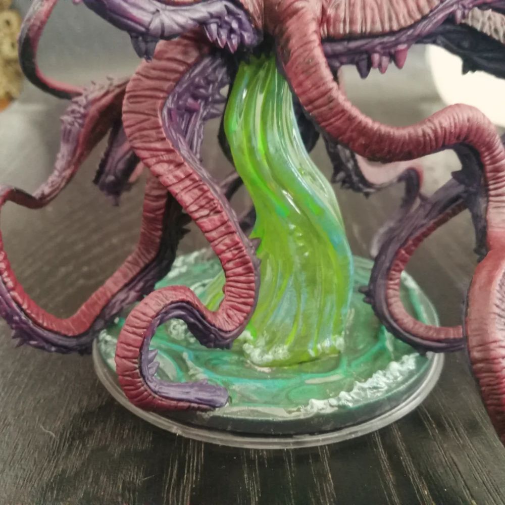 A closeup of the base, circular, partially transparent and painted to resemble green, stormy waters. Seafoam is detailed in white.