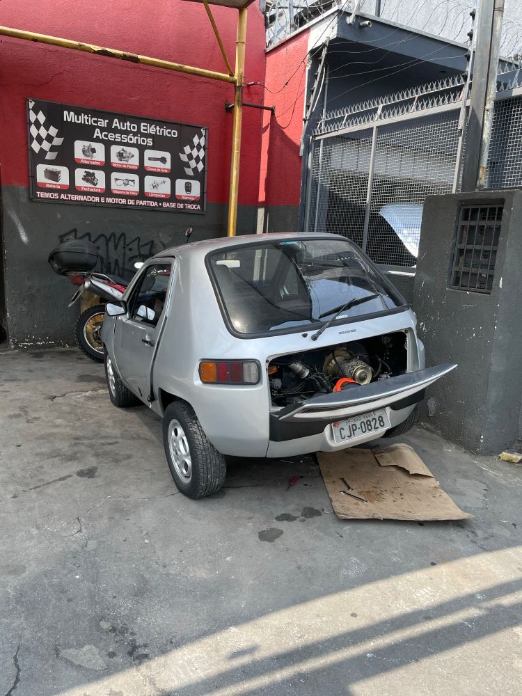 A silver Dacon 828, a microcar, seen from the rear with the engine bay open (it’s a rear engined car). 