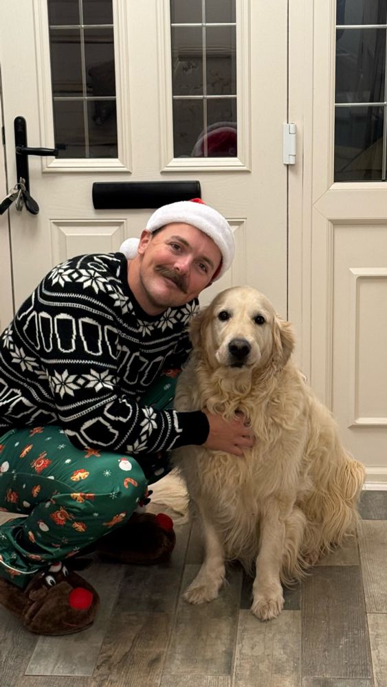 Sam in a Christmas jumper and funny pyjamas hugs his chonky golden retriever