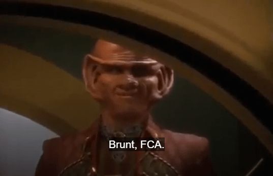 Ferengi behind a low arched doorway, subtitled "Brunt, FCA"
