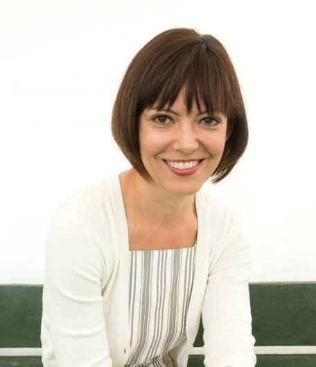 Dr Abigail Rokison-Woodall smiles at the camera against a bright background. She has shoulder length brown hair and wears a white top and cardigan.