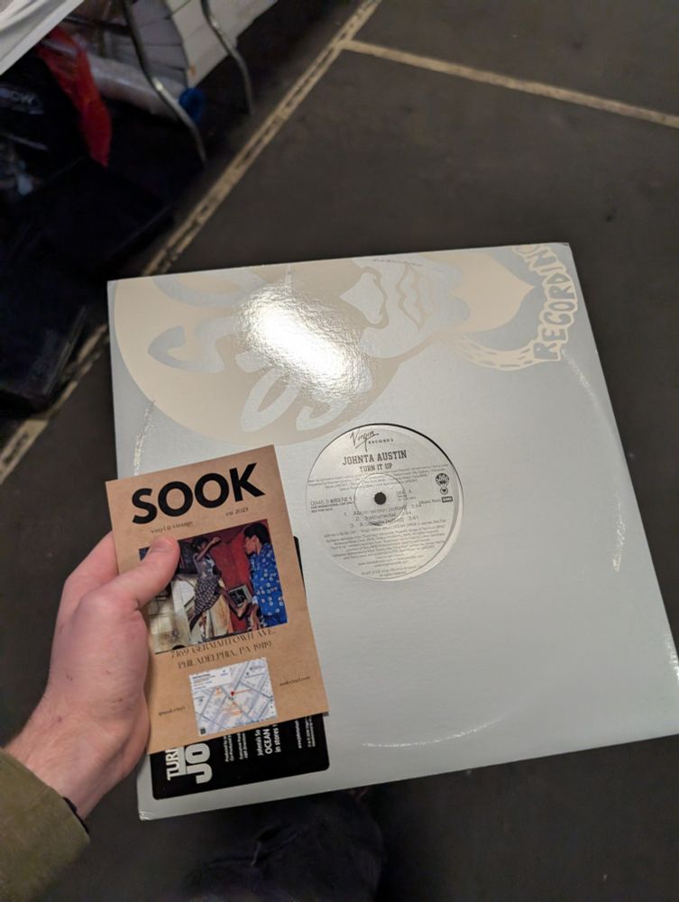 Man hand holding white record and sook record store flyer