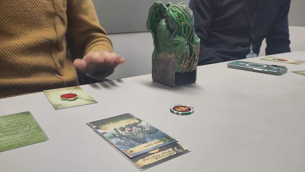 Une carte de Lovecraft letter vient d'être jouée. A coté une tour à dés Cthulhu bien plus grande que les cartes.