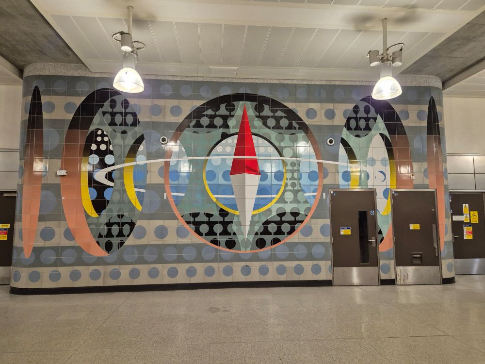 Tiles on a wall at a station. Two pendant lights. Tiled floor. 