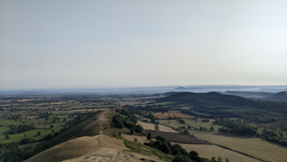 The view north from The Lawley, near Church Stretton, showing the Shropshire Plain and the distant Wrekin, under a banner cloud and a blue sky.