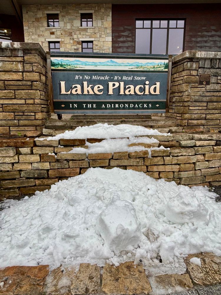 Pile of snow in front of sign for Lake Placid that reads, “It’s no miracle—it’s real snow!” 