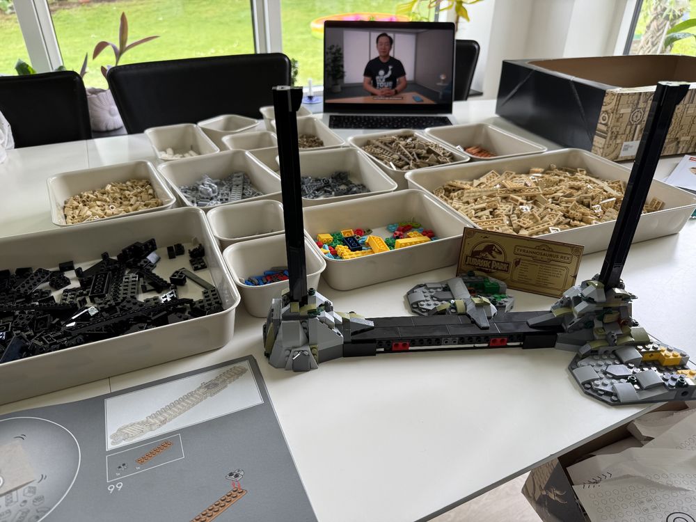 A bunch of boxes with Lego bricks and a computer showing a video in the background.