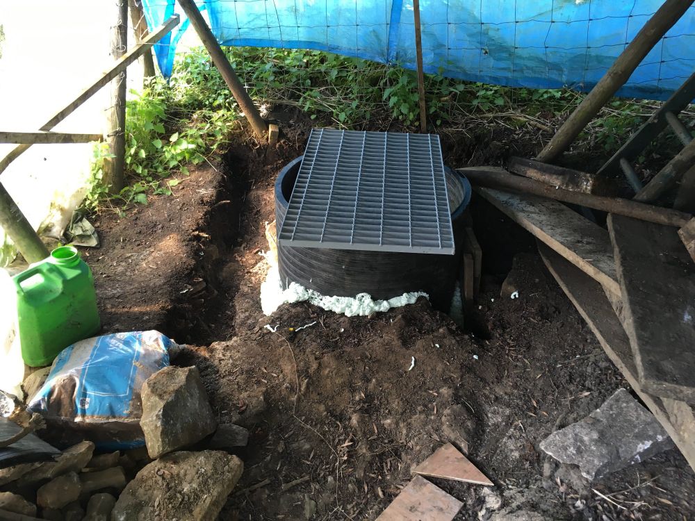 Top of pipe lined shaft with grill over.  In shelter of sheeting on wooden frame.

