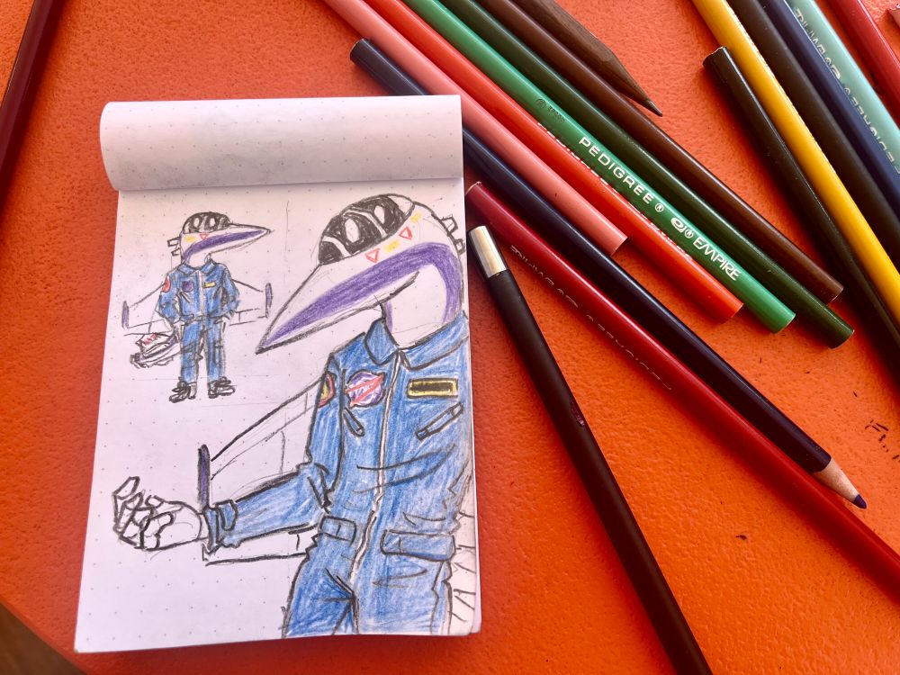 photo of a page with two colored pencil drawings of chase, an F-18 aeromorph in NASA livery and flight suit, on a dotted notepad.