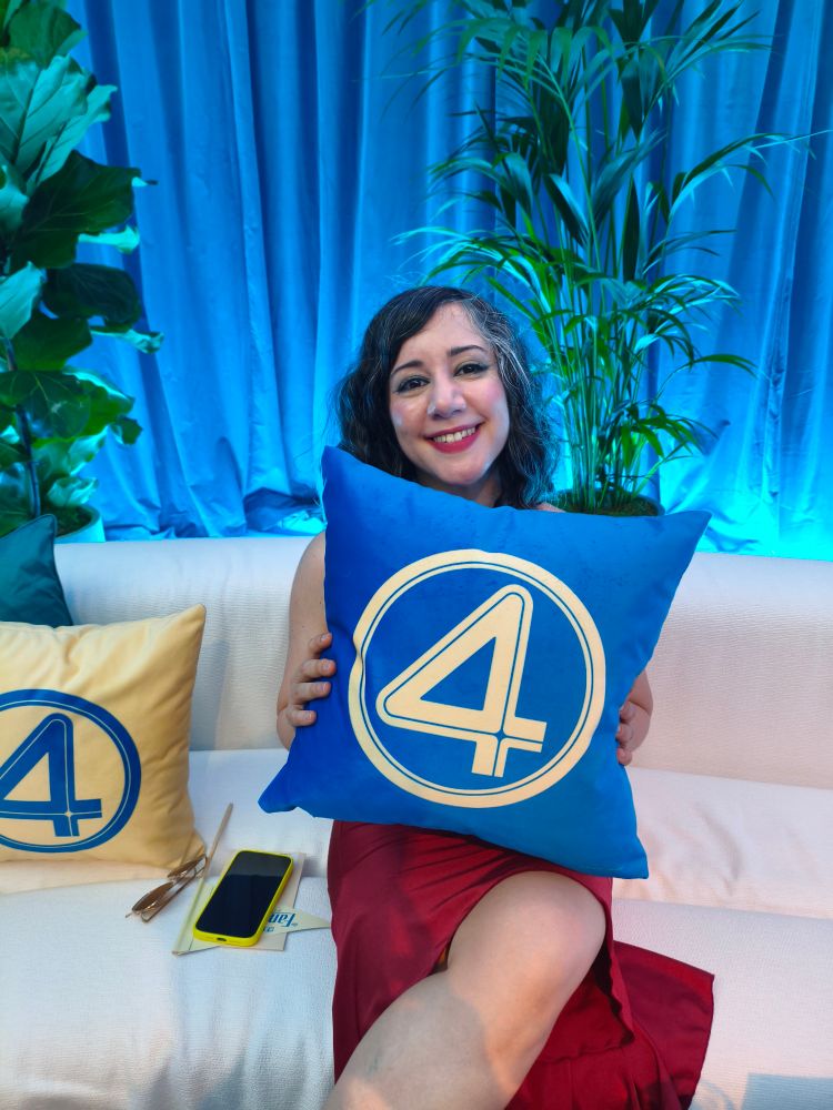 Laura, sonriente en un sofá, sostiene un cojín azul de Los Cuatro Fantásticos 