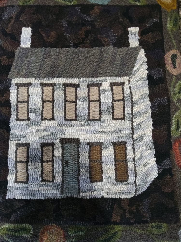 A carpet with a woven image of a white two-story house on it.