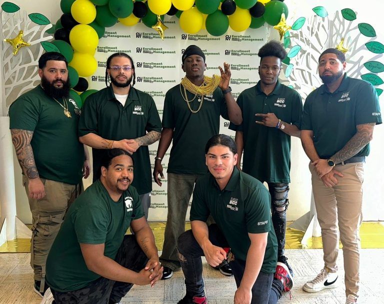 Group of seven individuals in green polo shirts, posed in front of a backdrop with balloons and a banner featuring logos of RWJ Barnabas Health.