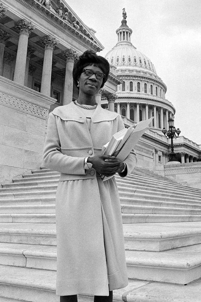 Shirley Chisholm holding papers poses in front of the Capitol.