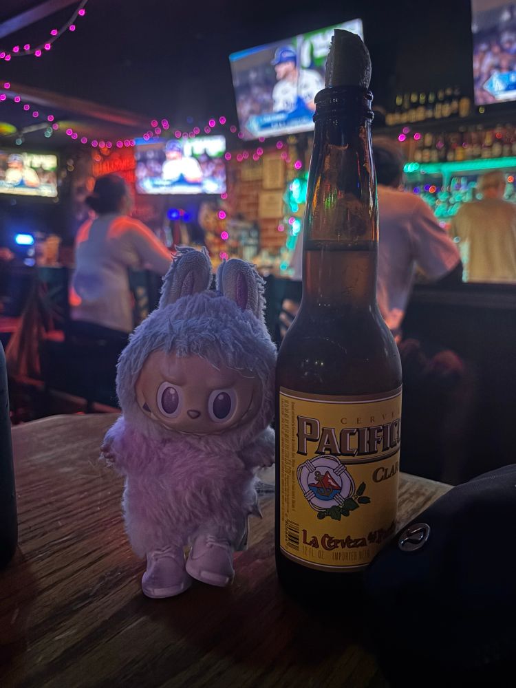 labubu next to a pacifico beer bottle in a dive bar