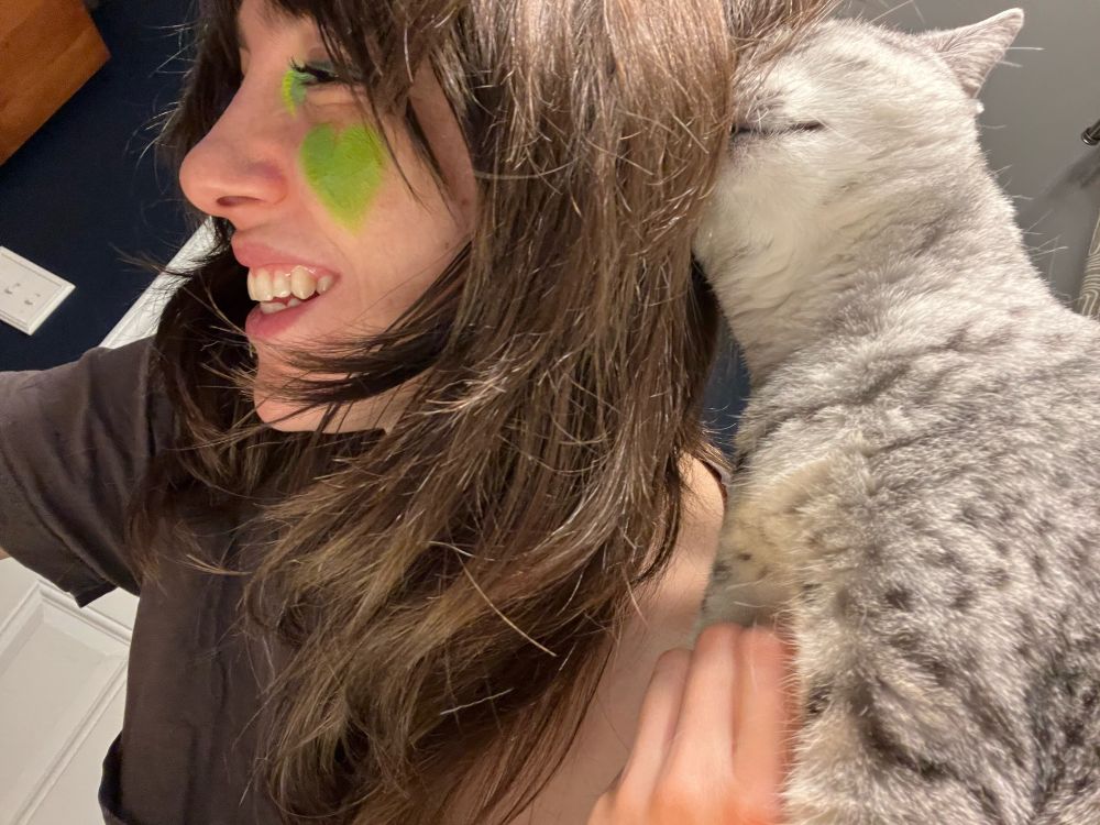 Yarrow sports some neon Turtle/heart makeup and a big grin while Jonesy, the cat, gets super into head-butting her human. 