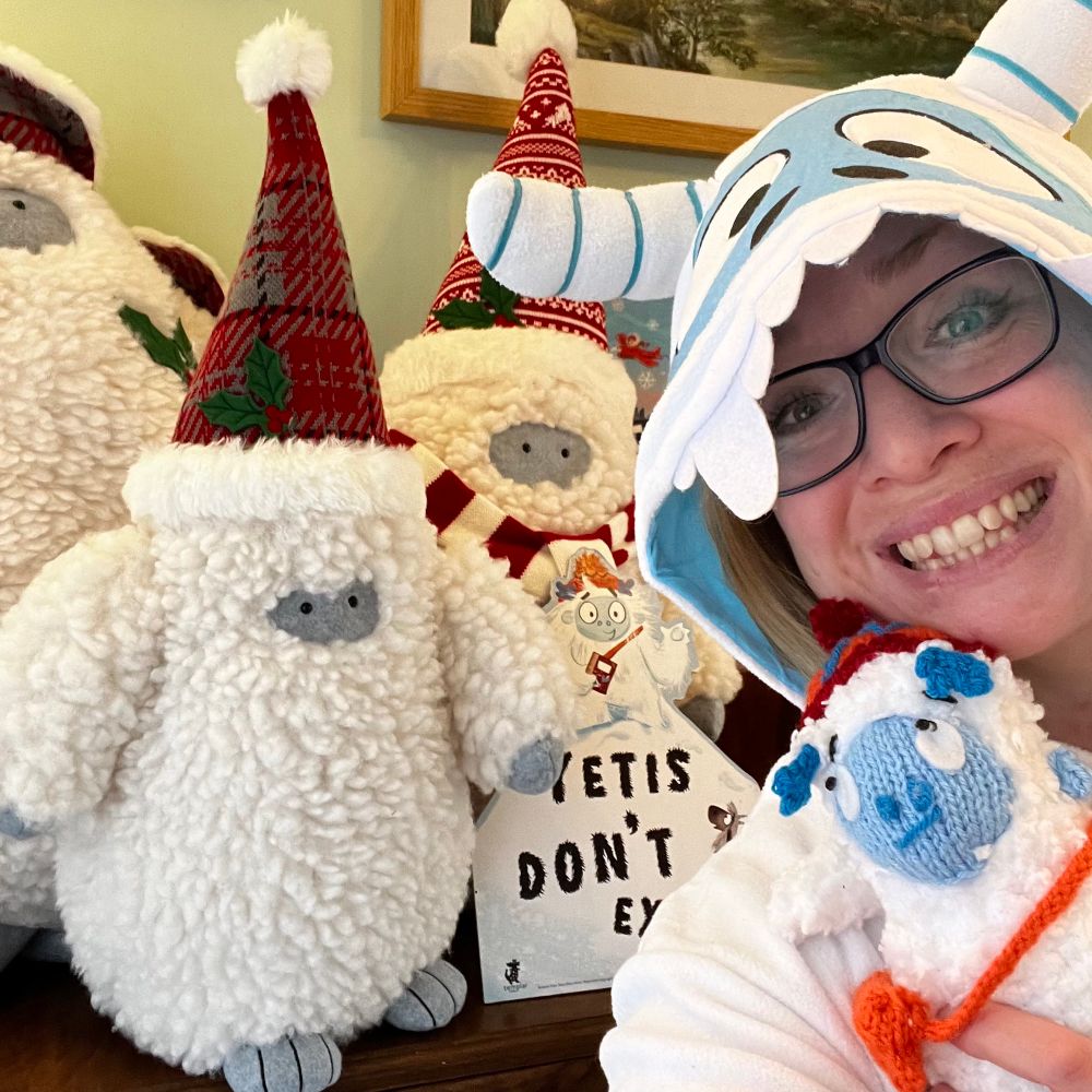 Kate Thompson, the author of Yetis Don’t Exist, posing in a magnificent yeti onesie with a collection of yeti toys otherwise known as a flurry of yetis.