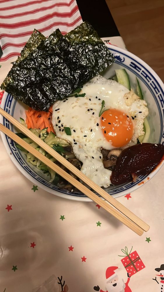 A bowl of bibimpap. It has seaweed, an omelette with sesame sprinkled. Some zucchini, cucumber, carrot, mushrooms, sprouts and guchojang bean paste.