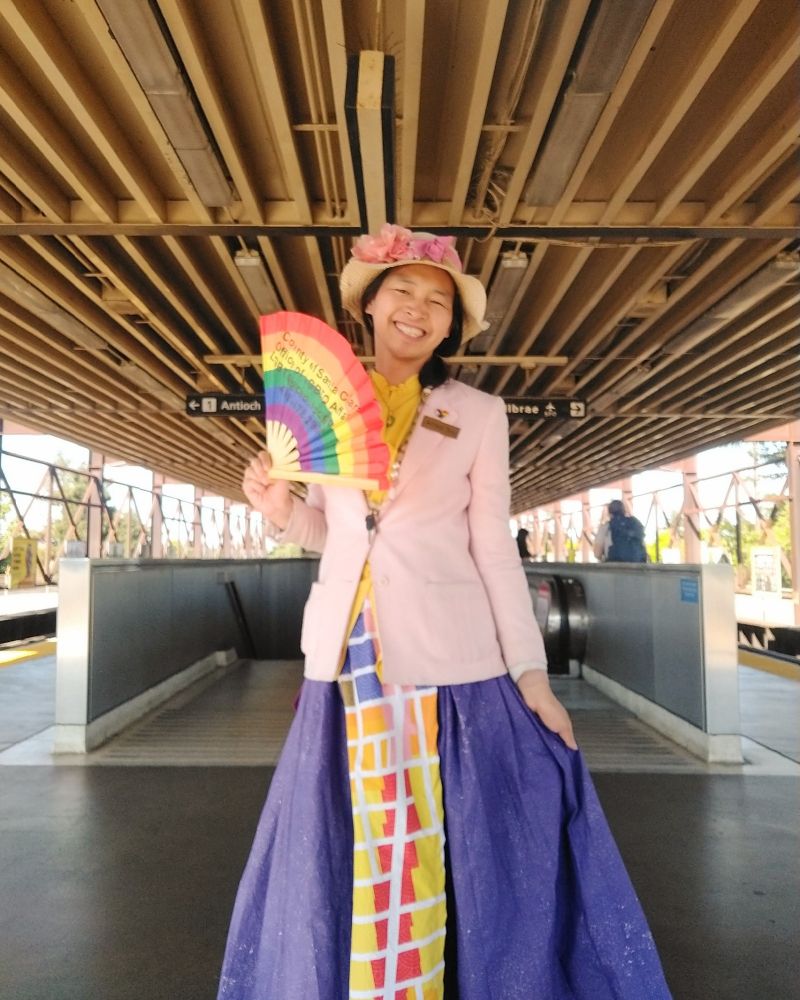 Alfred wearing a pink blazer and a long purple mamianqun-style skirt with a multicolored pattern down the front panel, which is based on Berkeley zoning map around telegraph avenue